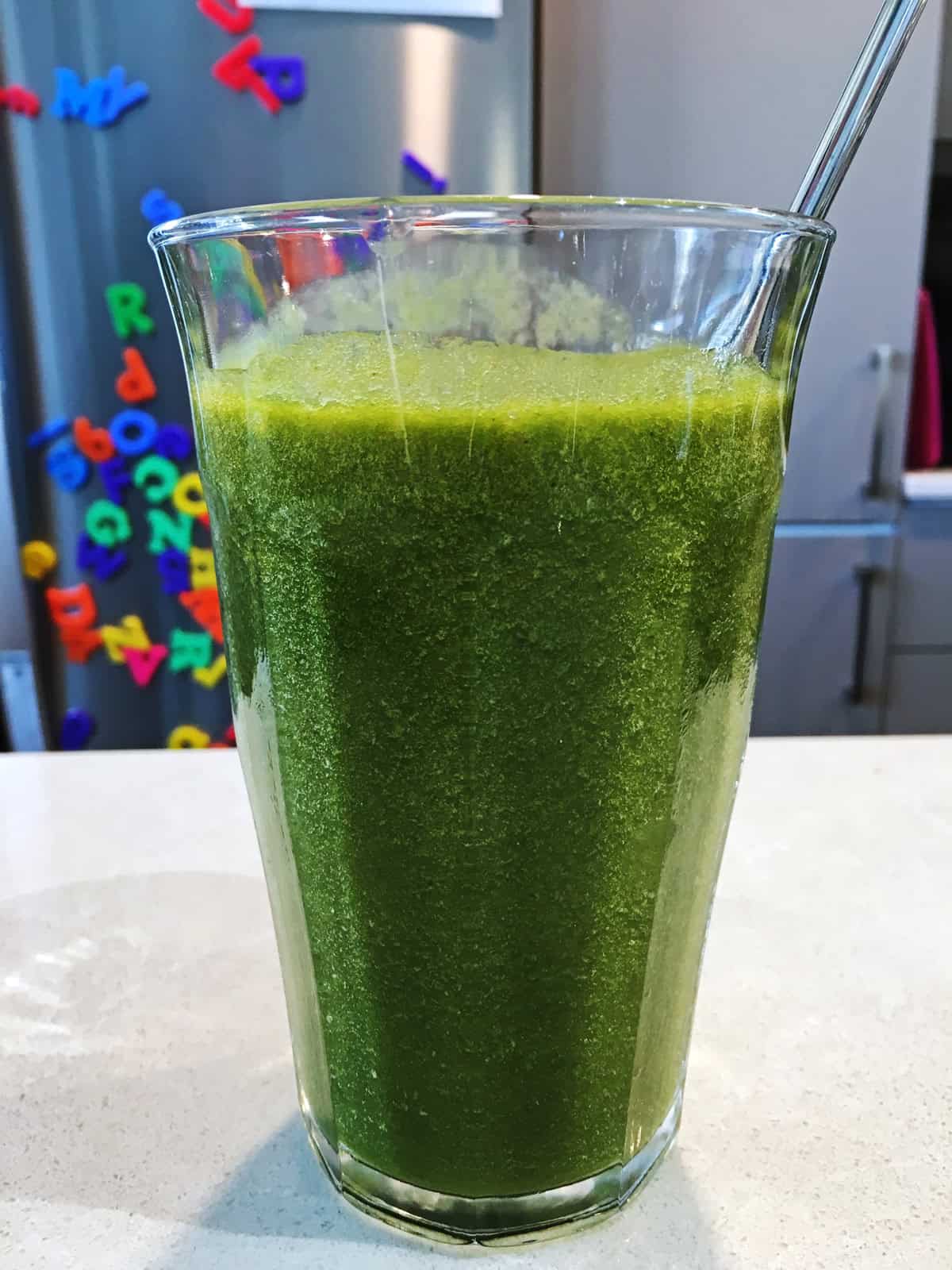 Green smoothie in a tall glass with a metal straw.