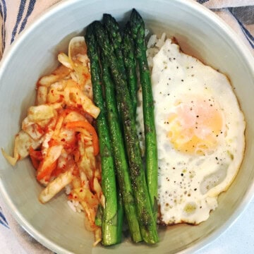 Kimchi breakfast bowl with asparagus and eggs in an off-white ceramic bowl.