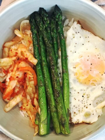 Kimchi breakfast bowl with asparagus and eggs in an off-white ceramic bowl.