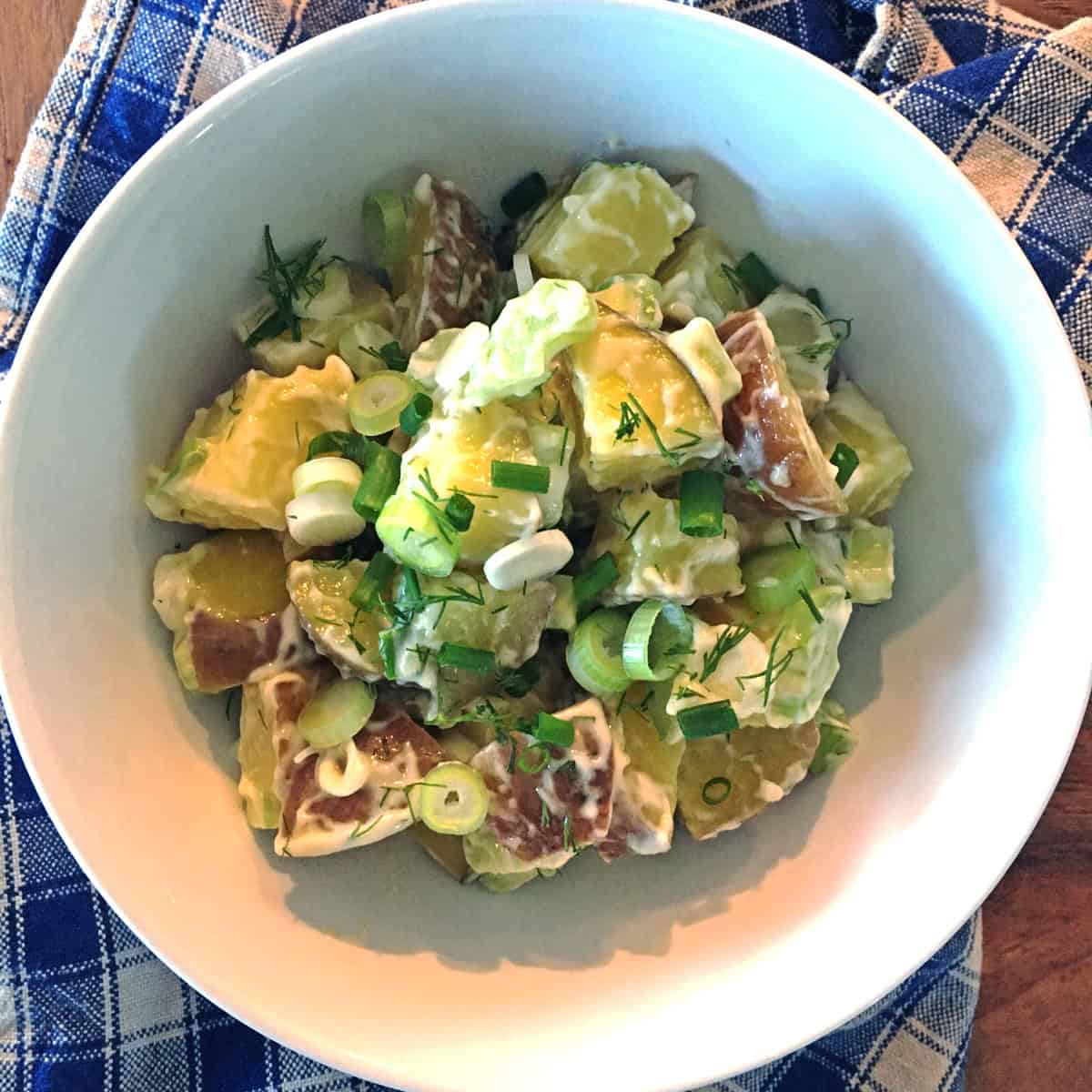 Red potato salad with dill in a white salad bowl.
