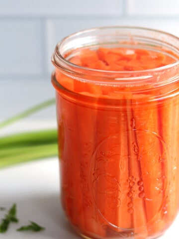 Fermented carrots in a Mason jar on a white marble countertop.