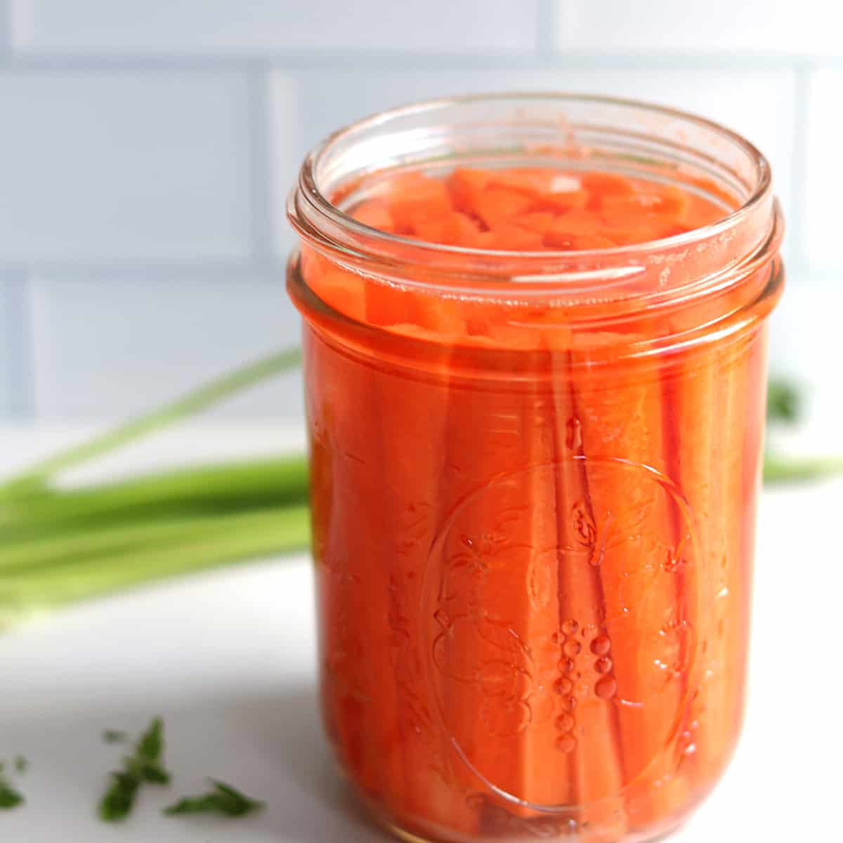 Fermented carrots in a Mason jar on a white marble countertop.