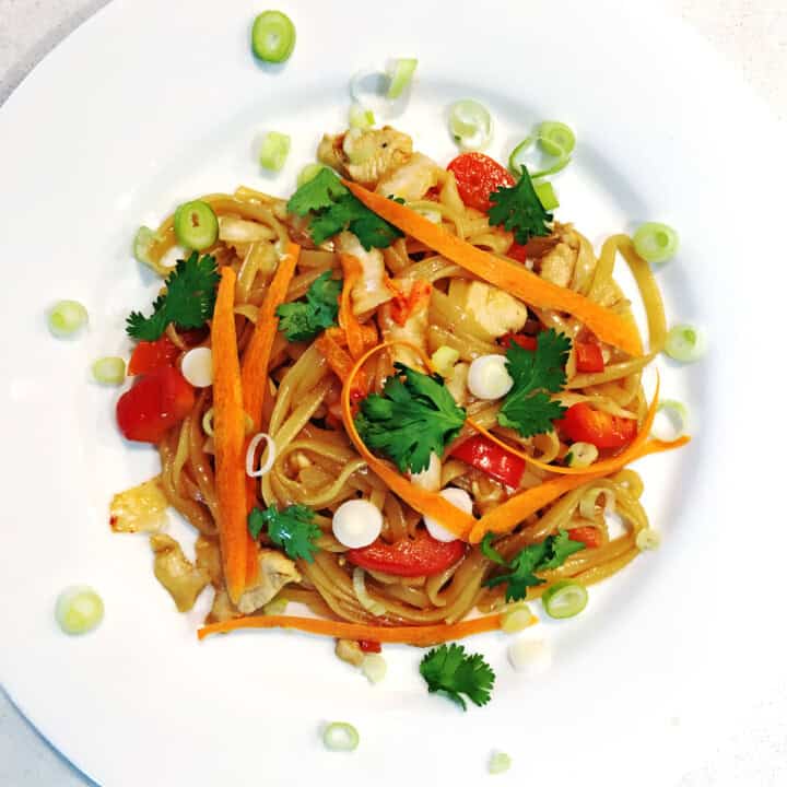 Kimchi noodles garnished with fresh cilantro and scallions on a white plate.