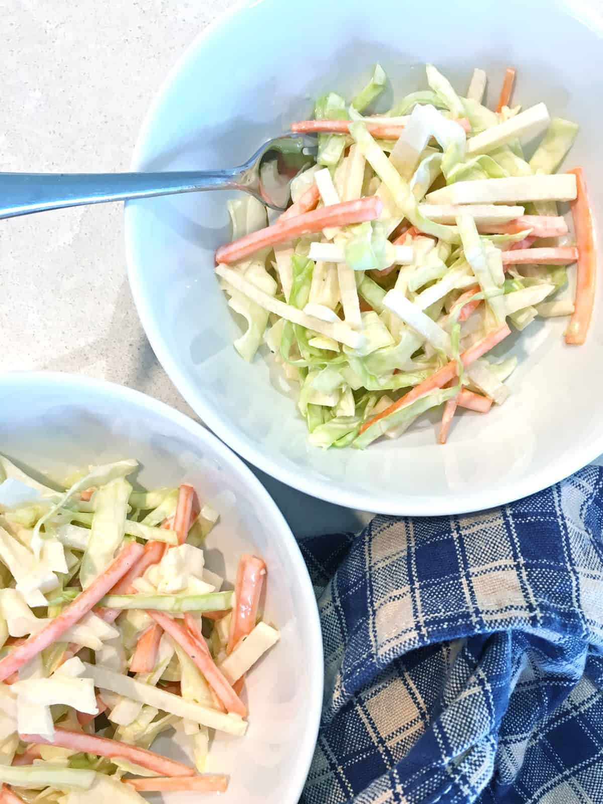 Simple jicama slaw in two small white salad bowls with a plaid navy and tan napkin.