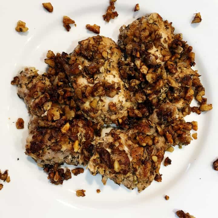 Herb and walnut crusted chicken thighs on a white plate.
