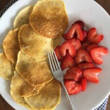 Mini almond flour crepes with fresh sliced strawberries and a fork on a white plate