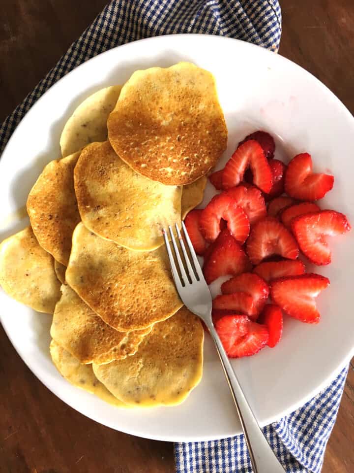 Mini almond flour crepes with fresh sliced strawberries and a fork on a white plate