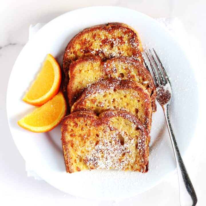 French toast with fresh orange slices on a white plate.