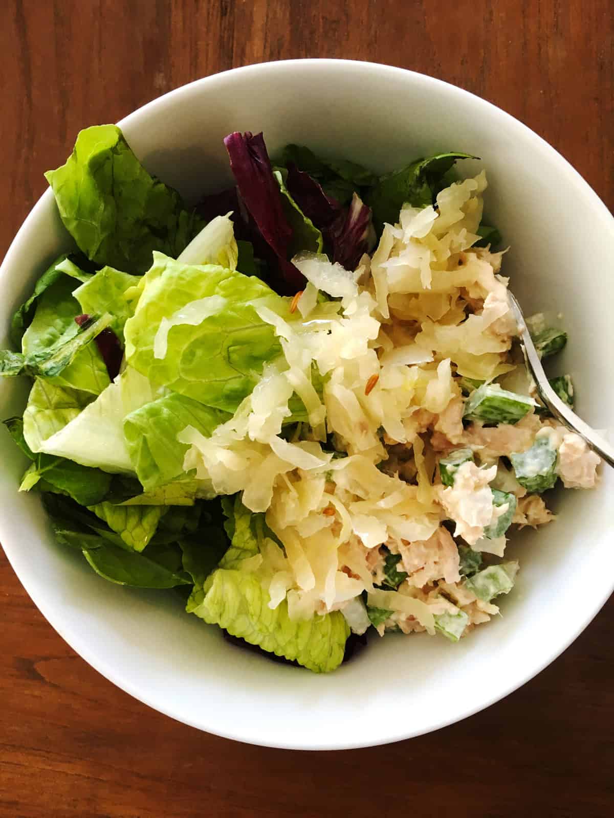 Tuna sauerkraut salad in a white serving bowl on a brown wood table.