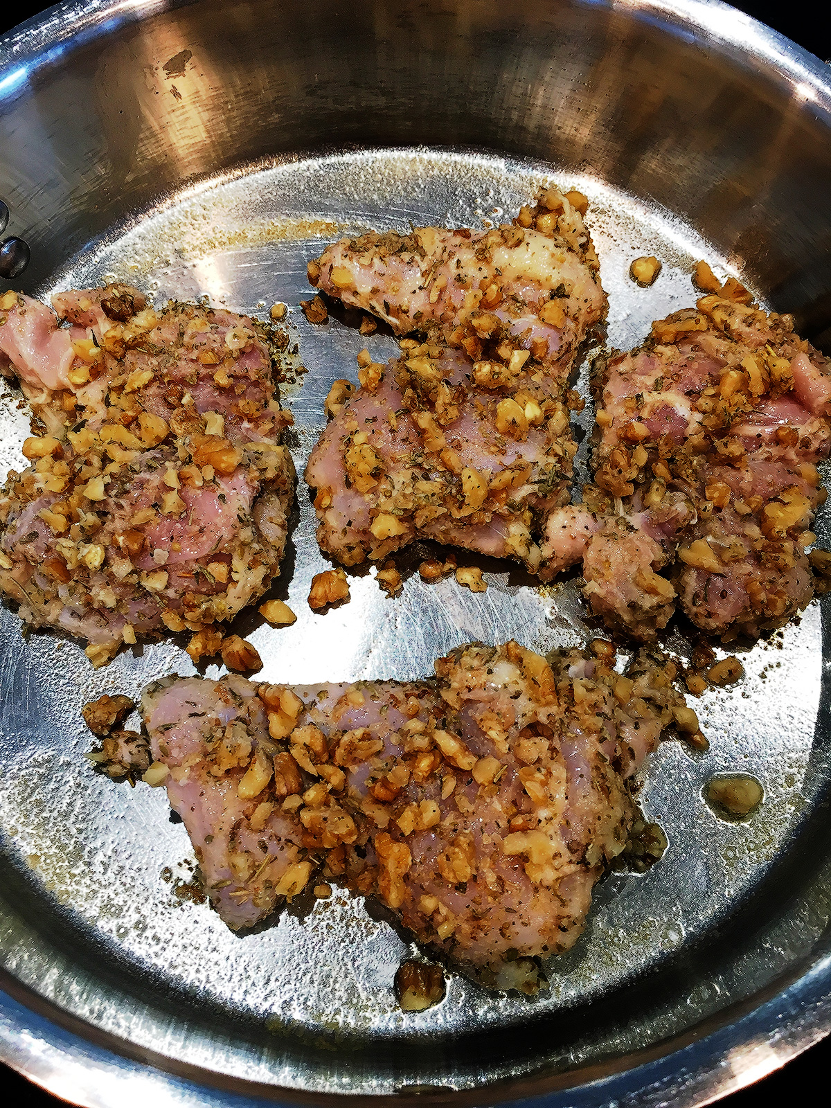 Cooking four chicken thighs with walnuts and herbs in a stainless steel skillet.