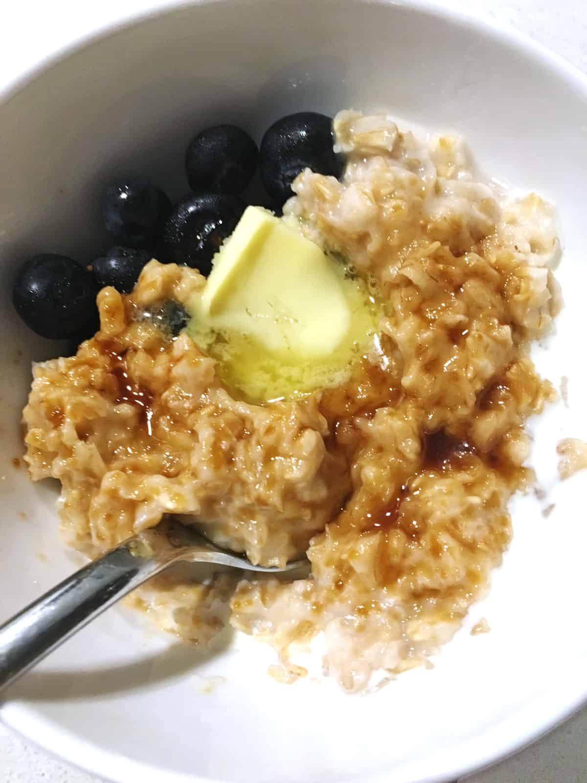 Oatmeal with blueberries and cream in a white bowl with a silver spoon.