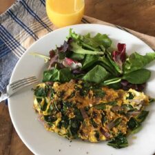 Dandelion greens omelette with mixed salad greens on a white plate with glass of orange juice
