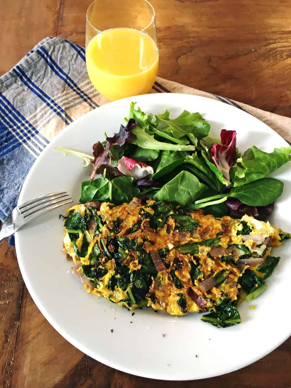 Dandelion greens omelette with mixed salad greens on a white plate with glass of orange juice