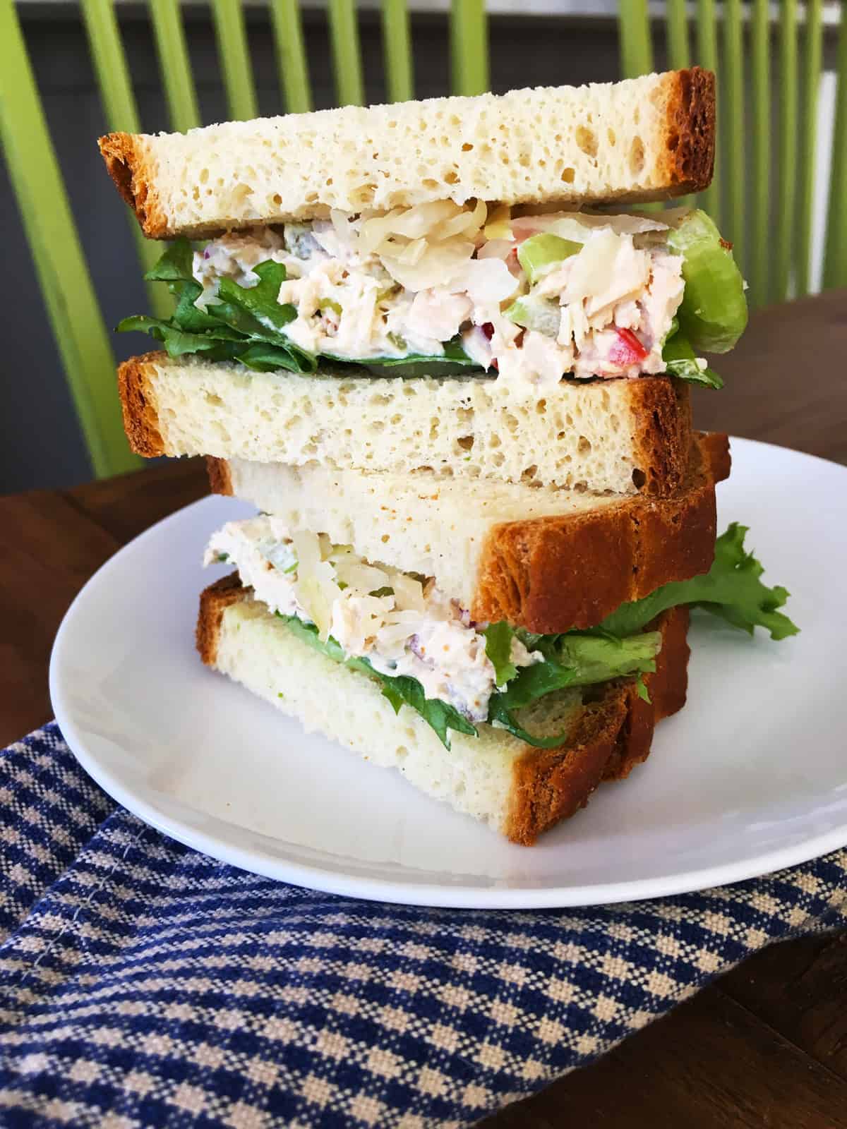 Tuna salad and sauerkraut sandwich on a white plate with a blue and tan plaid napkin.