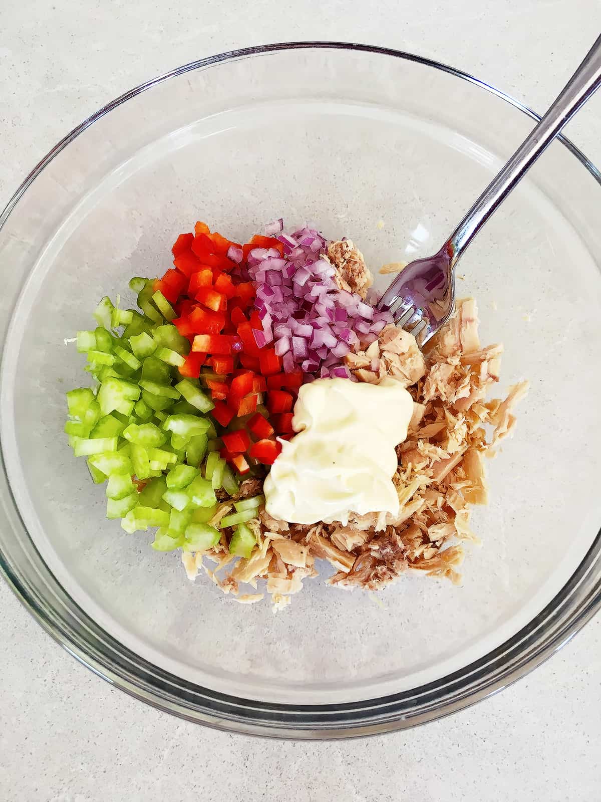 Chopped veggies with mayonnaise and tuna in a glass mixing bowl