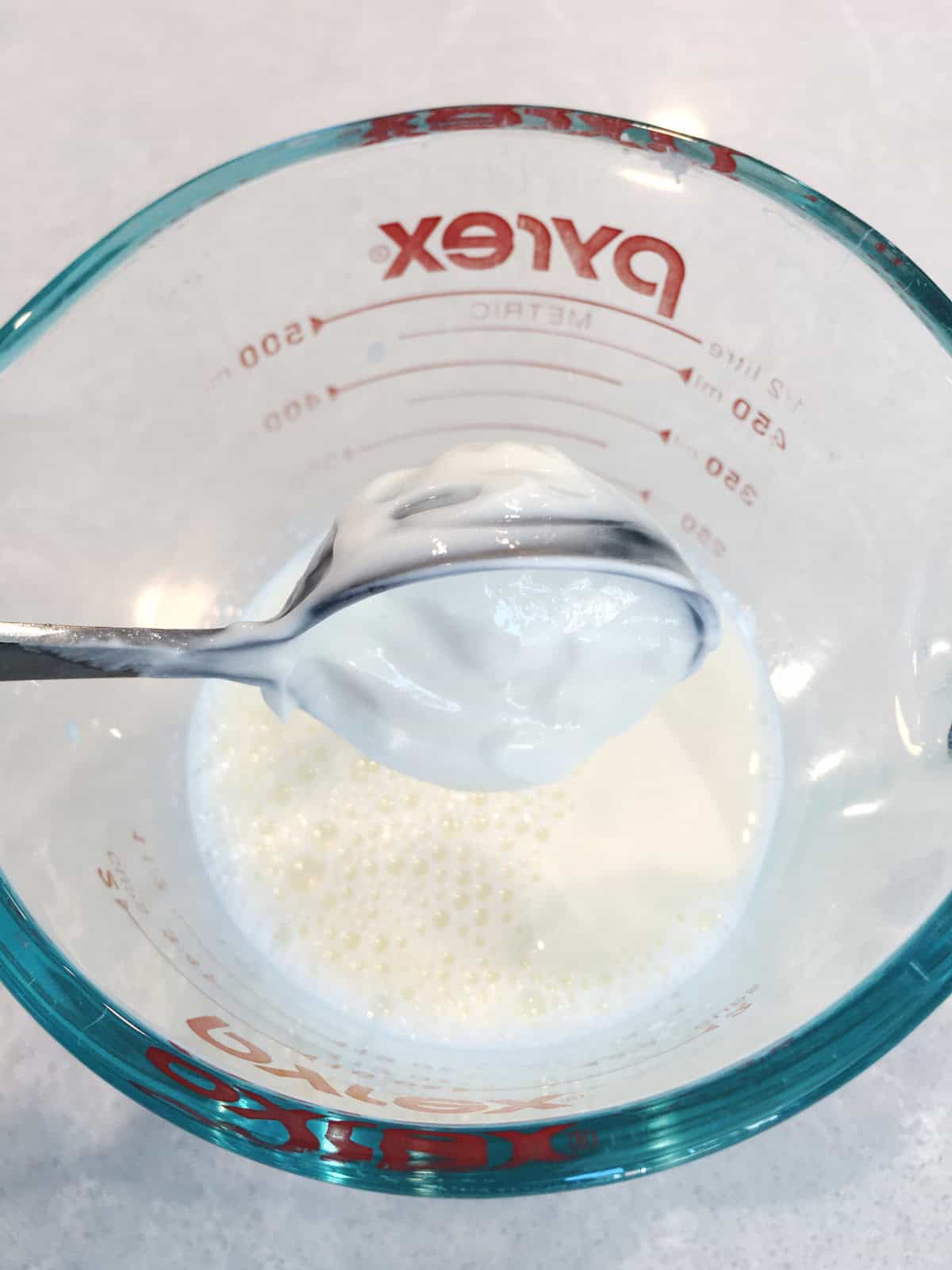 Adding yogurt cultures into a glass measuring cup of milk