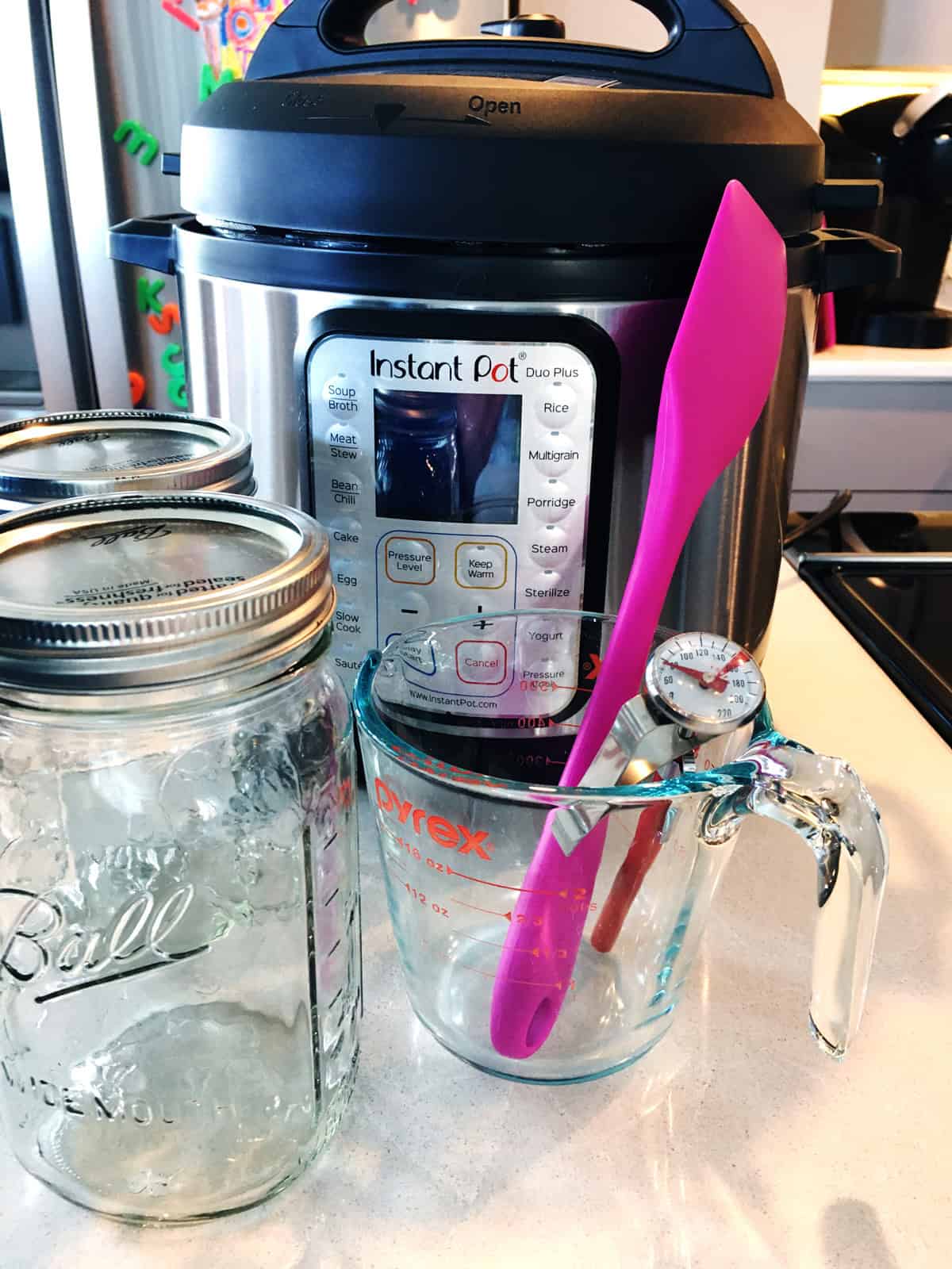 Instant Pot, mason jars, measuring cup, spatula and thermometer on a light grey countertop