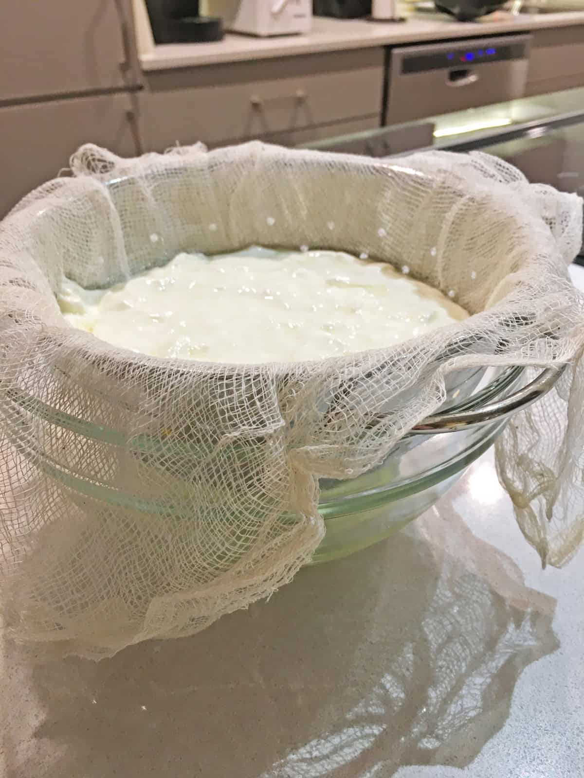 Fresh yogurt straining over a cheesecloth-lined colander and glass mixing bowl