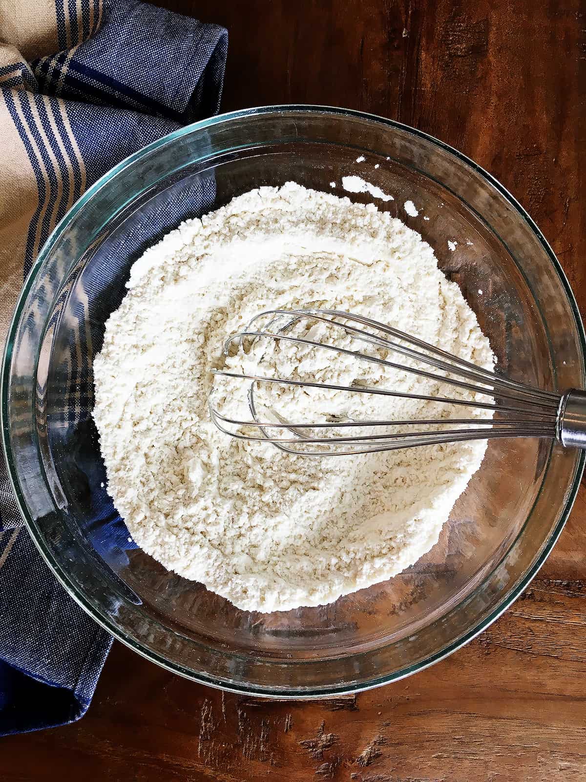 Flour and dry ingredients in a glass bowl with a silver whisk