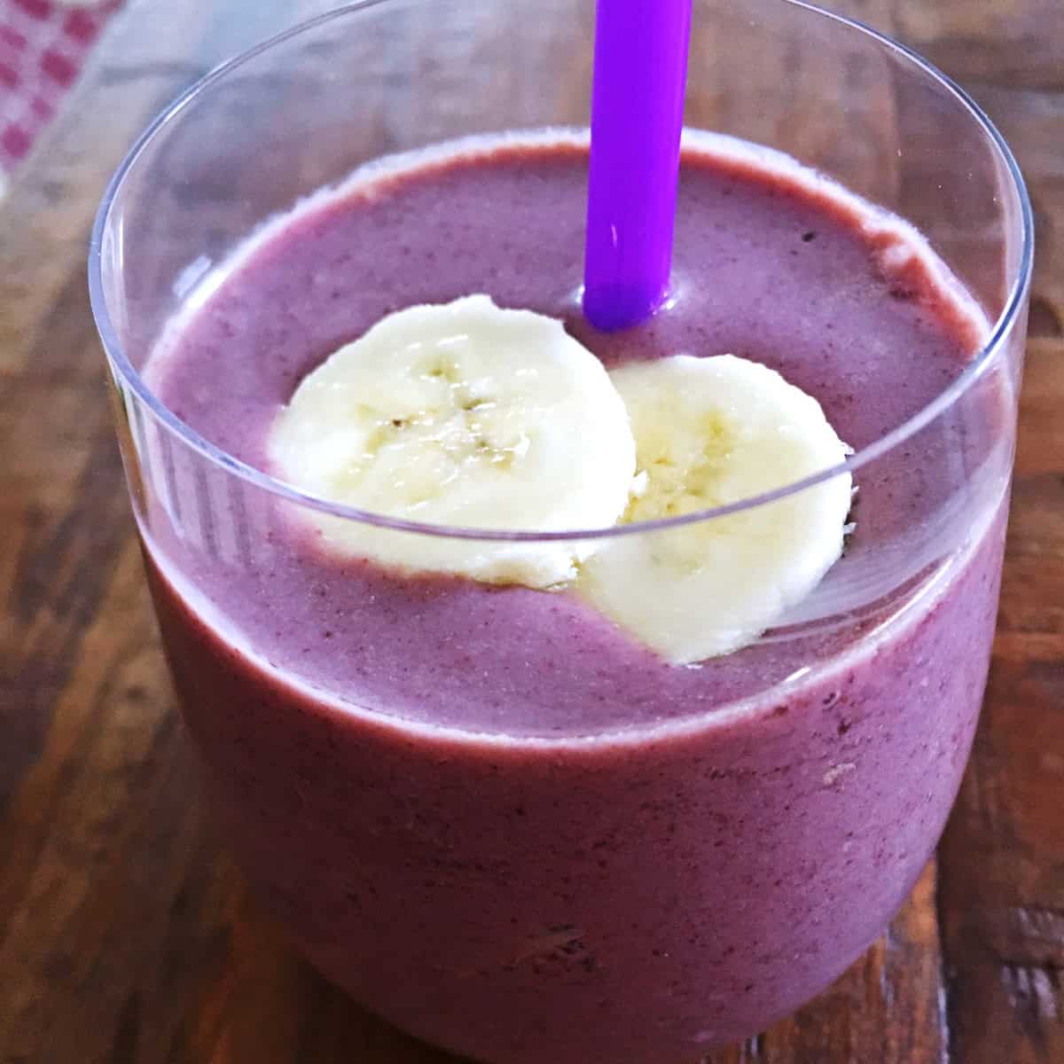 Açaí berry smoothie and a purple straw topped with banana slices.