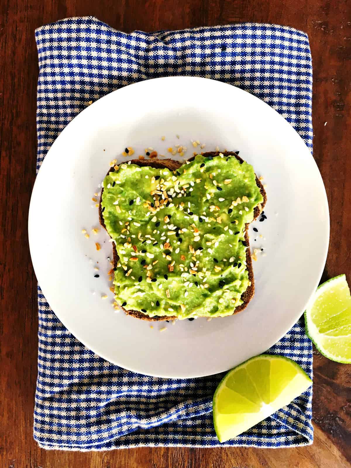 Avocado toast with everything bagel toppings on a white plate atop a blue and tan checkered napkin.