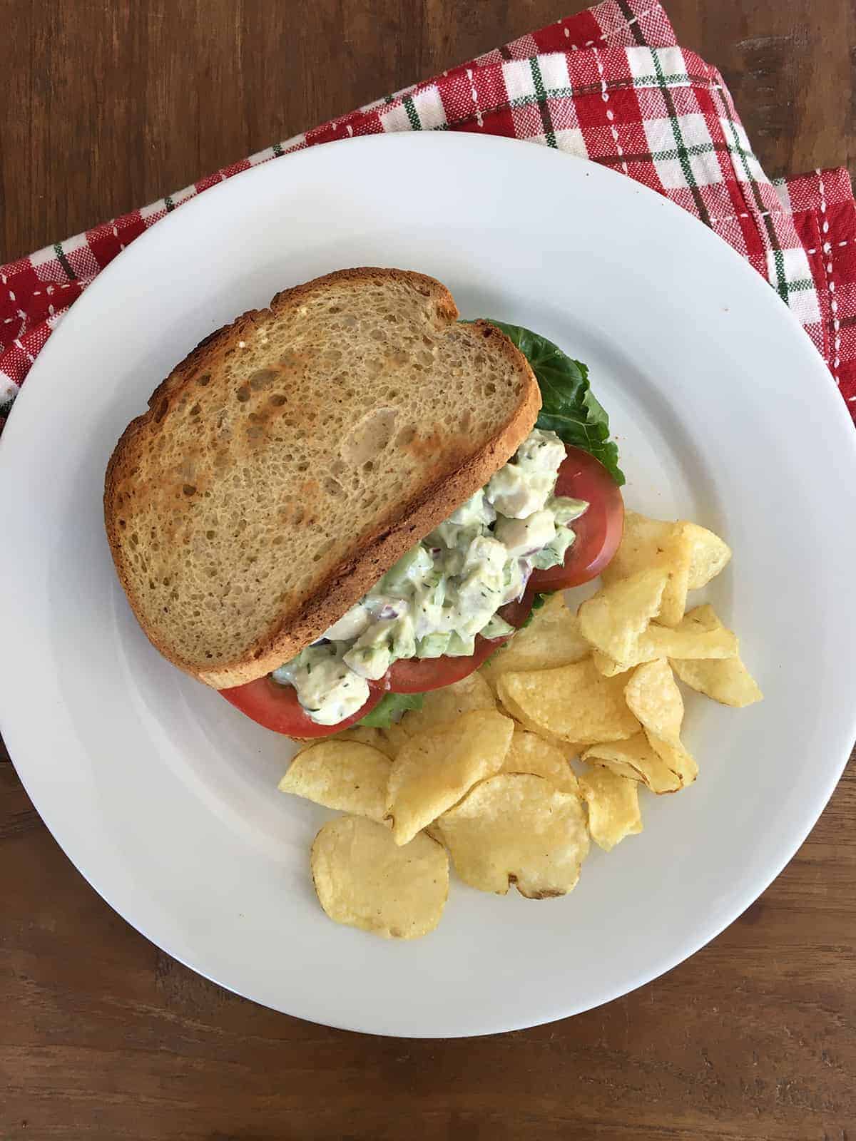 Chicken salad with avocado in a sandwich with toasted whole-grain bread, sliced tomatoes and Romaine lettuce and a side of potato chips