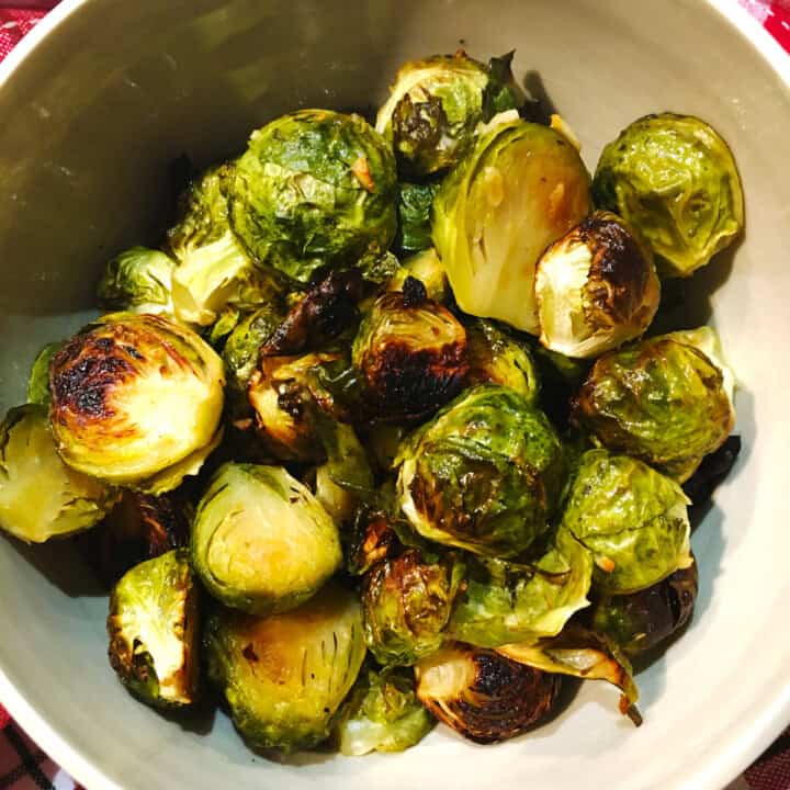 Roasted Brussels sprouts in a tan ceramic serving bowl.