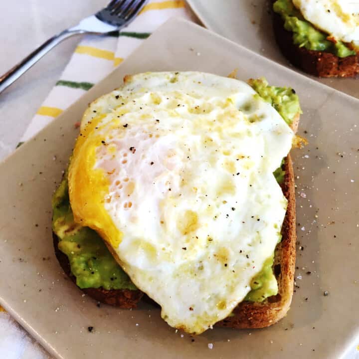 Avocado toast with egg on tan ceramic plates.