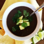 Black bean soup topped with avocado and cilantro in a white bowl