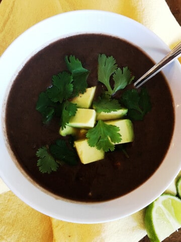 Black bean soup topped with avocado and cilantro in a white bowl