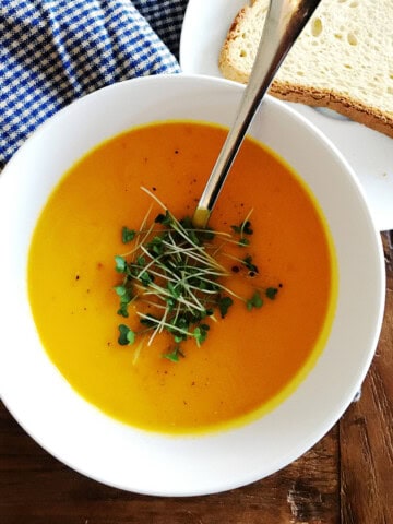 Carrot ginger soup topped with microgreens in a white bowl.