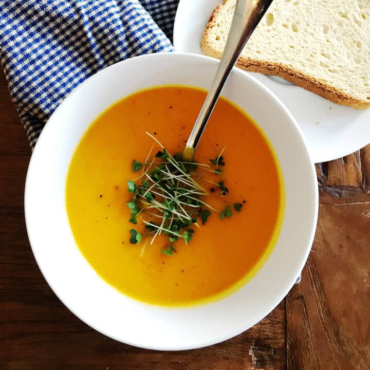 Carrot ginger soup topped with microgreens in a white bowl.