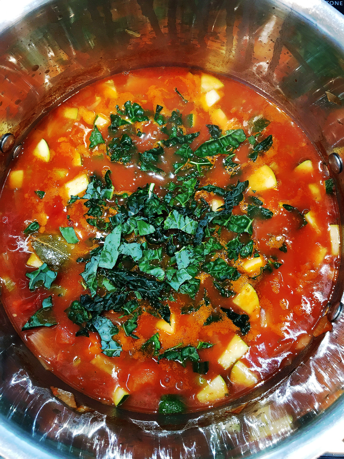 Minestrone soup in a large soup pot with fresh chopped kale pieces