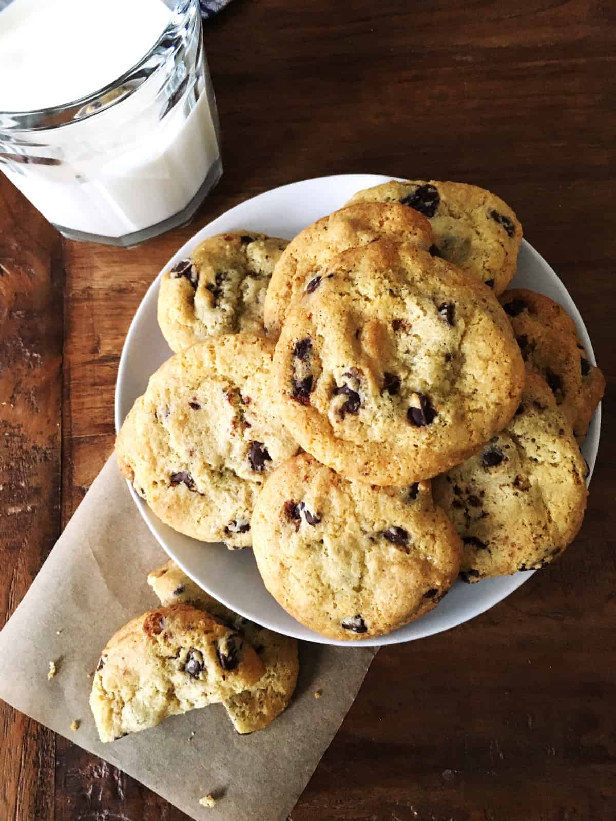 Gluten-free chocolate chip cookies with a glass of milk on a brown table.