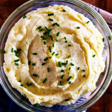 Homemade mashed potatoes garnished with parsley in a glass bowl.
