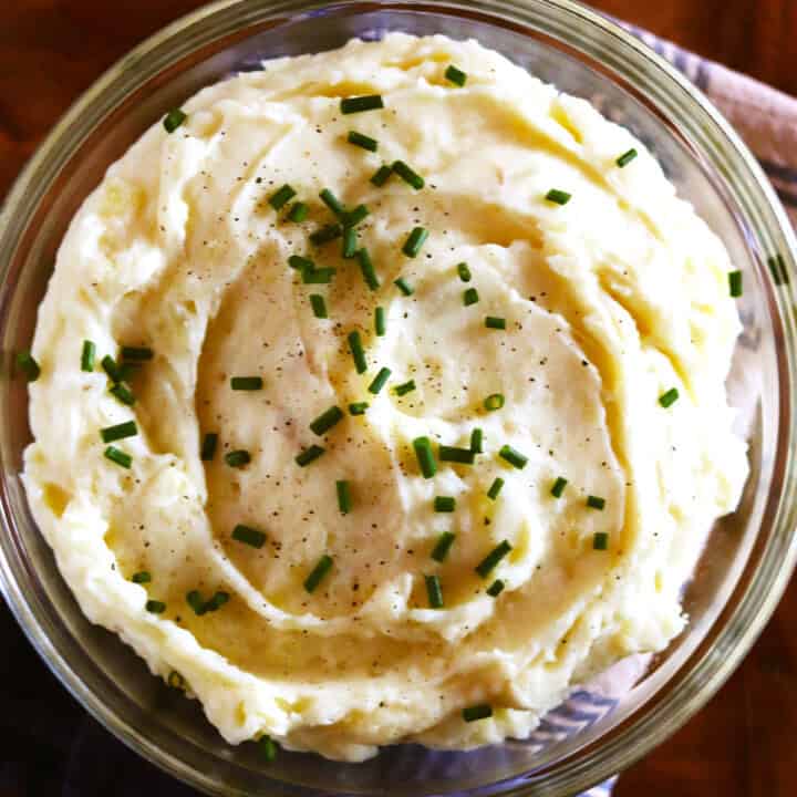 Homemade mashed potatoes garnished with fresh chives in a glass bowl.