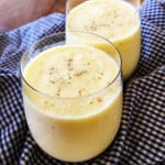 Two mango lassi drinks topped with cardamom