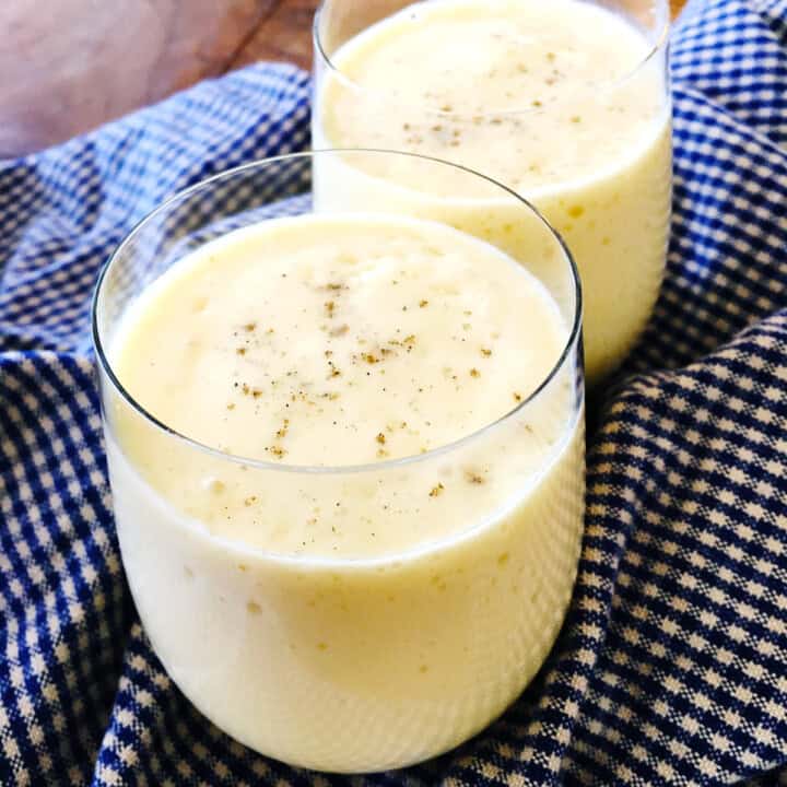 Two mango lassi drinks topped with cardamom.