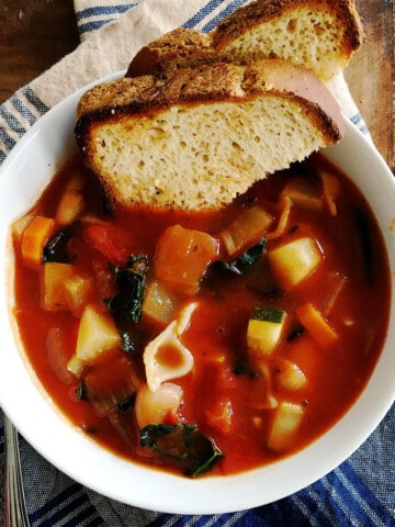 Minestrone soup and toasted bread in a white bowl.