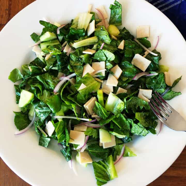 Cold cut salad with sliced chicken, red onions and cucumbers on a white plate.