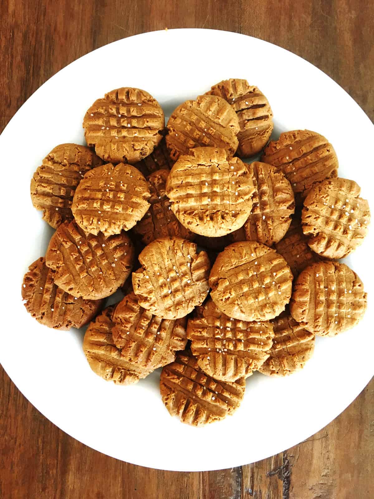 3 ingredient peanut butter cookies on white plate atop a brown table.