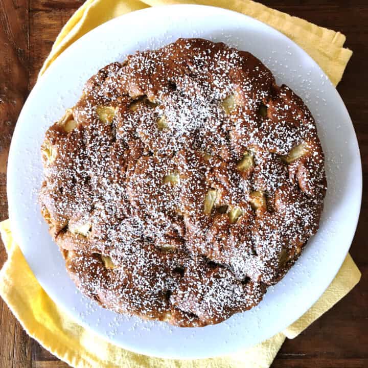 Apple cake dusted with powdered sugar on a white plate.