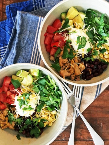Two citrus chicken burrito bowls with a blue and tan striped napkin.