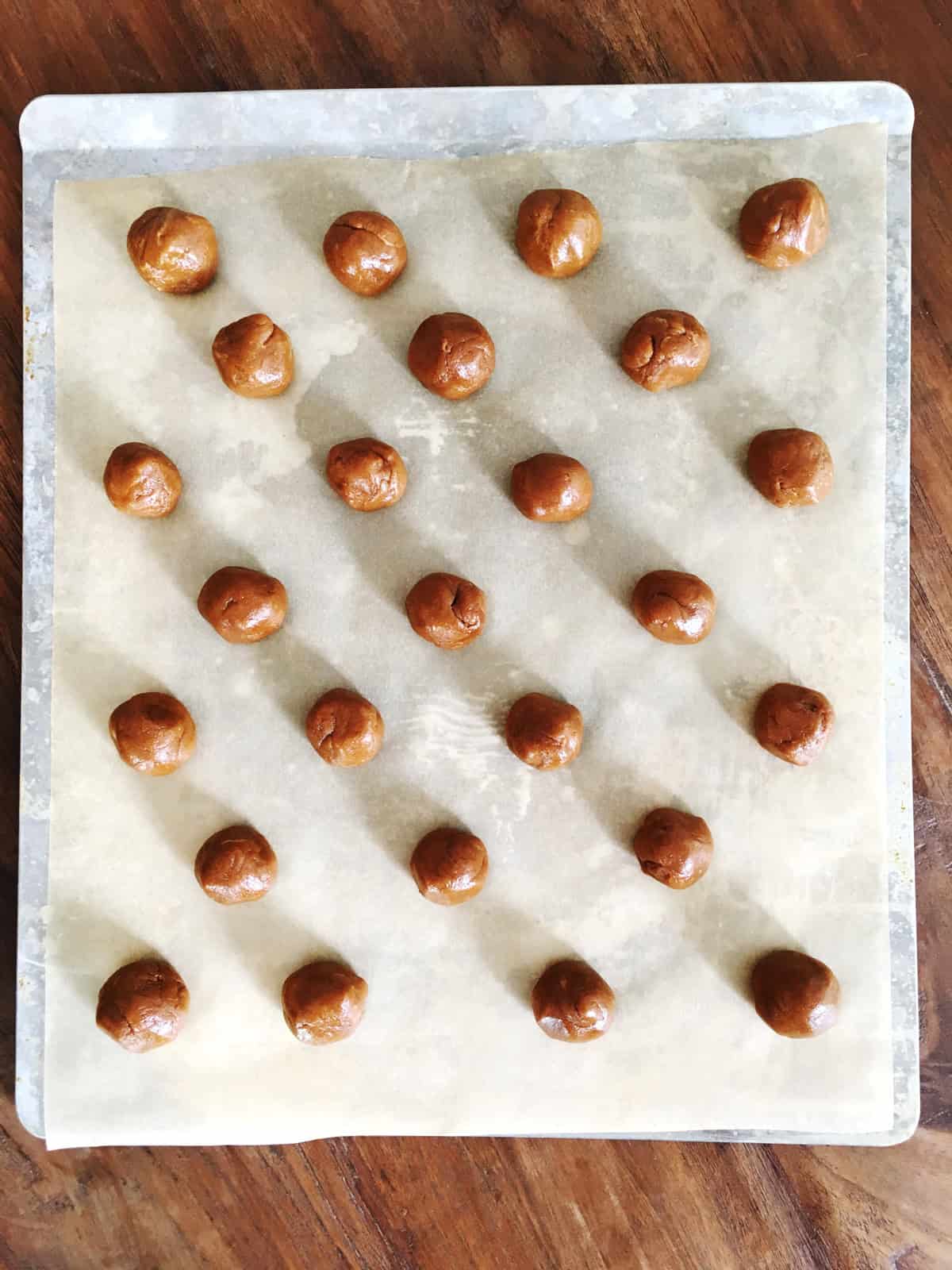 Peanut butter cookie dough balls on a stainless steel baking sheet lined with parchment paper.