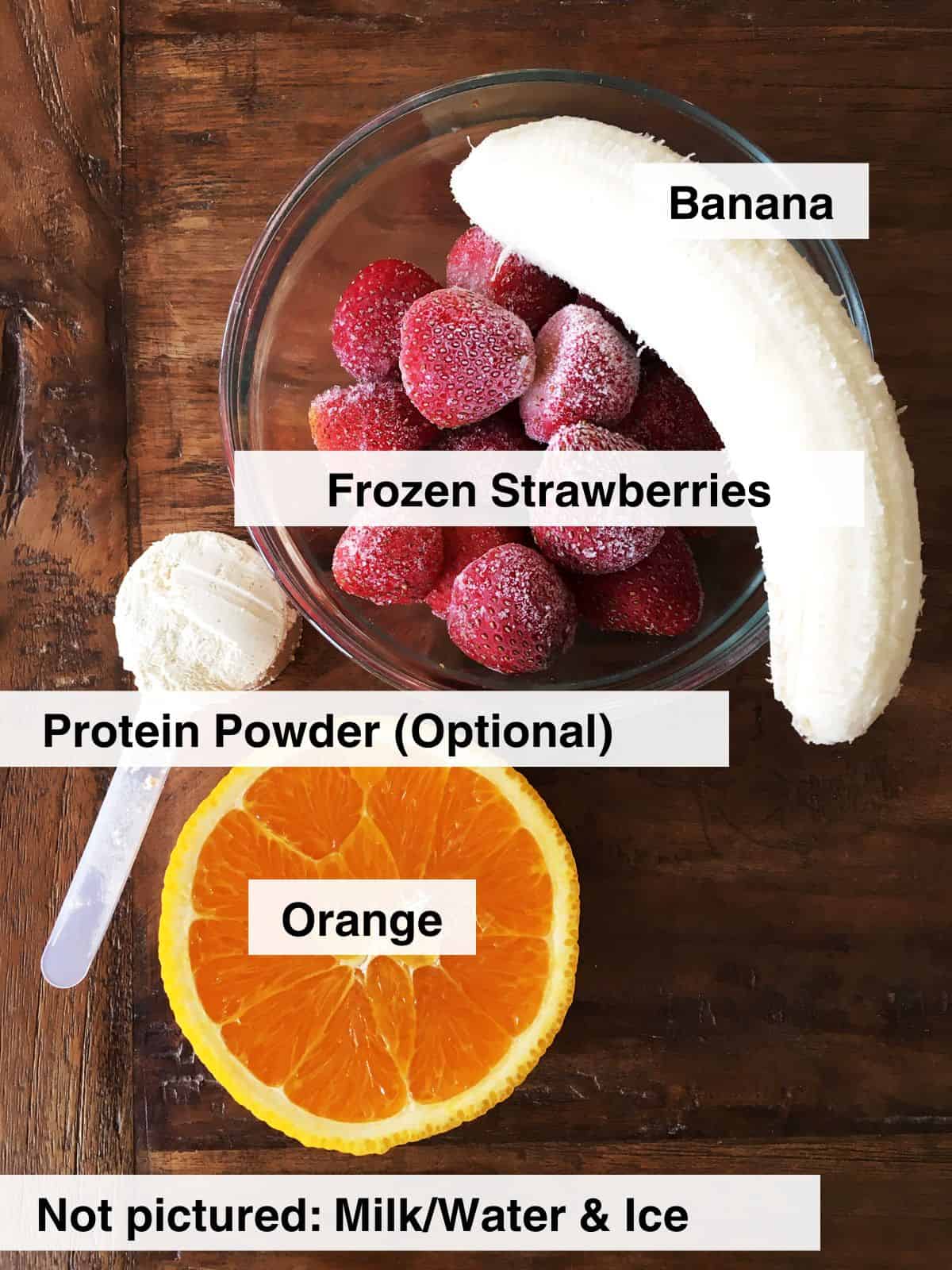 Frozen strawberries, peeled banana, half an orange and a scoop of protein powder on a brown wood table