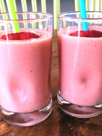 Two strawberry banana smoothies with green and blue straws.