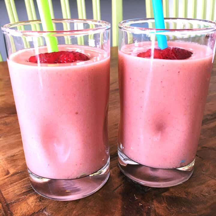 Two strawberry banana smoothies with green and blue straws.