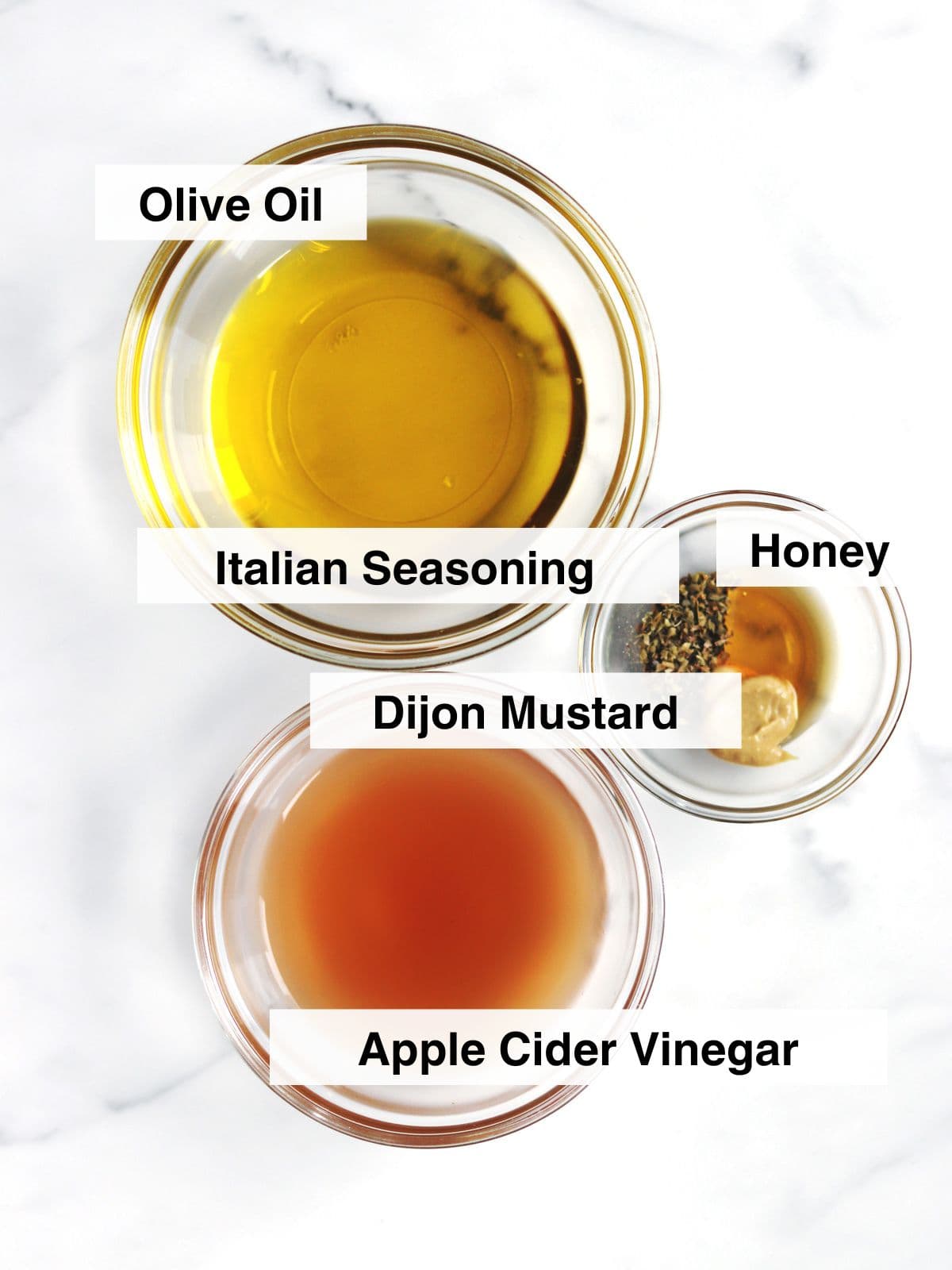 Apple cider vinegar, olive oil and Italian seasoning jars laying on a brown wood table