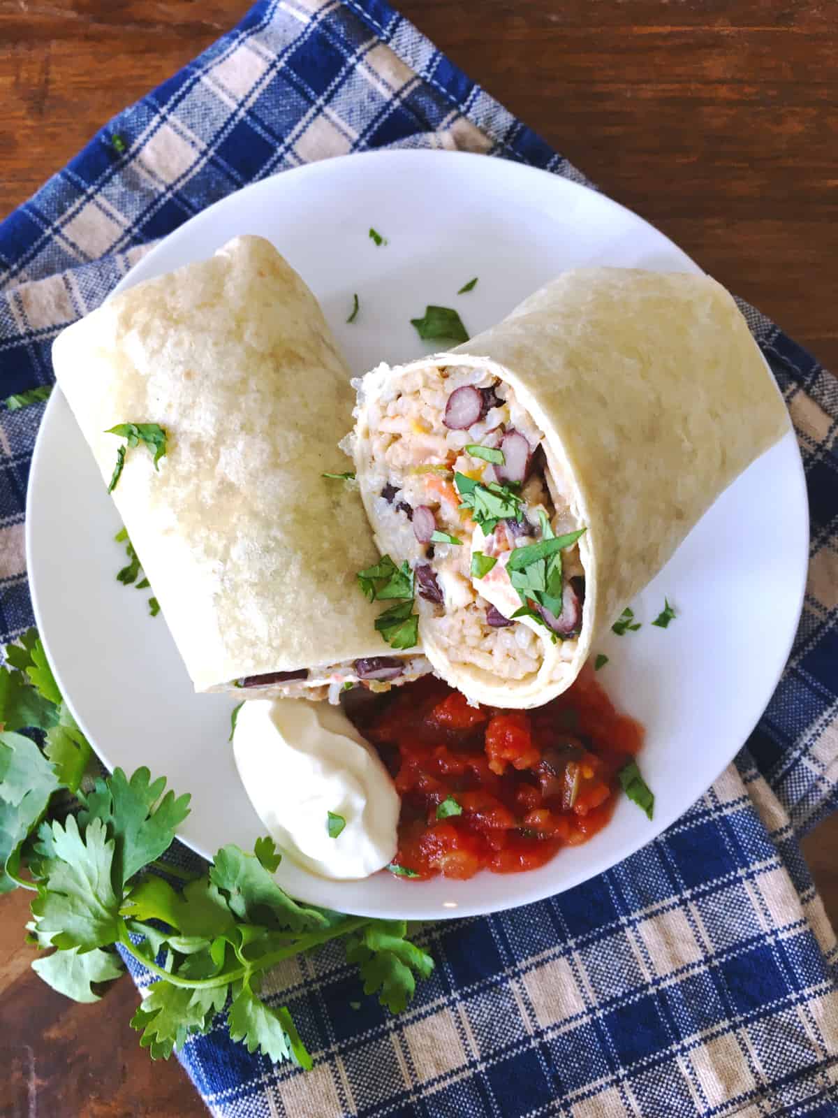 Chicken burrito with salsa and sour cream on a white plate with a blue and tan checkered napkin.