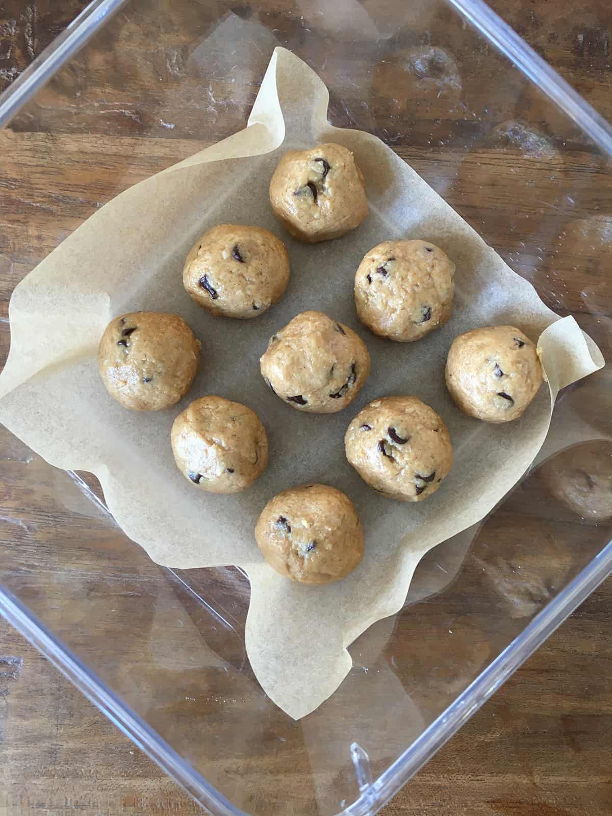Peanut butter protein balls in a glass Tupperware container lined with parchment paper